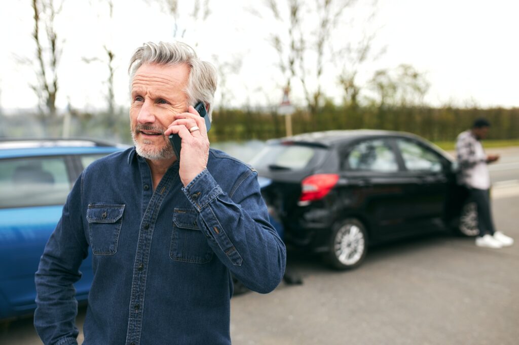 Senior Male Driver Calls Car Insurance Company On Mobile Phone After Traffic Accident